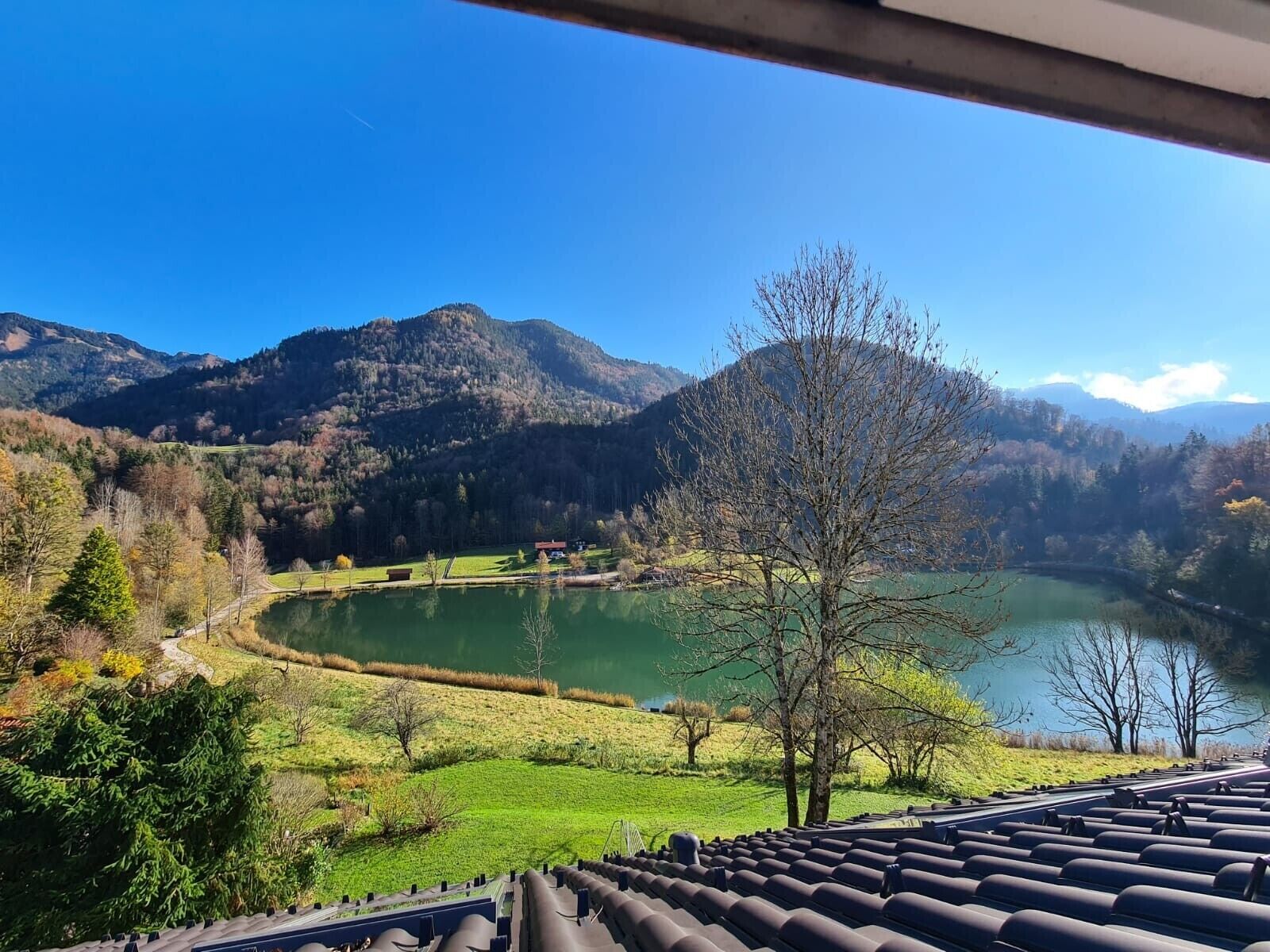 Vista de un lago rodeado de montañas, cielo despejado y un sendero que conduce a un edificio con techo.