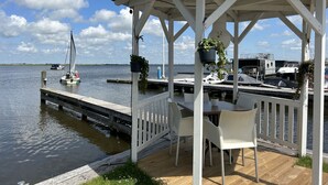 A gazebo with a table and chairs, overlooking a calm body of water with a sailboat in the distance. - Penthouse by Interhome (Uitgeest)
