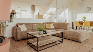 A modern living room with a sectional sofa, a wooden coffee table, and a dining area with yellow chairs. - Penthouse by Interhome (Uitgeest)
