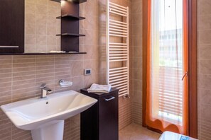 Une salle de bain équipée d’un lavabo, d’un porte-serviettes et d’une fenêtre avec des stores.