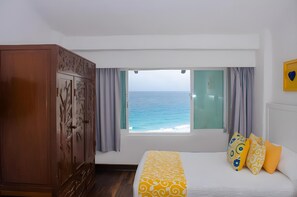 Un dormitorio con un ventanal grande, una cama con ropa de cama estampada, un armario de madera y vista al mar.