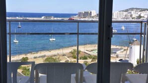 Un balcón con vista al mar, barcos y edificios al fondo.