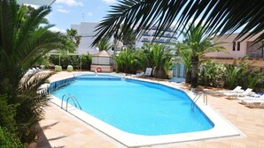 Una piscina con sillones de descanso y palmeras.