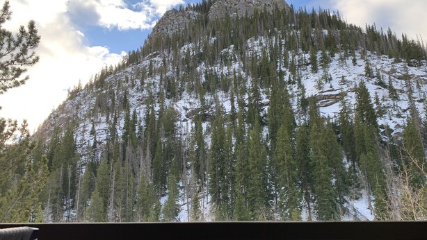 A mountain with a rocky peak, surrounded by evergreen trees and patches of snow.