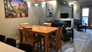 A dining area with a wooden table and chairs, a sofa, a television, and a fireplace.