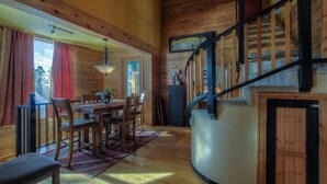 A wooden interior with a dining area, staircase, and a view of the outdoors.