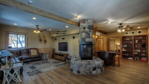 A cozy living room with a stone fireplace, leather sofa, wooden beams, and a bookshelf.