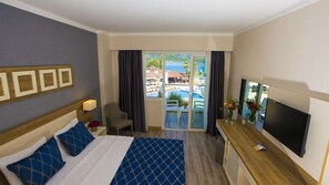 Una camera d'albergo con un letto, una scrivania con televisione, una sedia e vista sulla piscina e su un'area esterna.