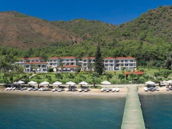Un resort con diversi edifici, un lungo molo che si protende sull'acqua e un paesaggio montuoso sullo sfondo.