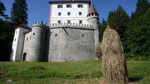 A castle with a central tower, a round tower, and a haystack in the foreground.