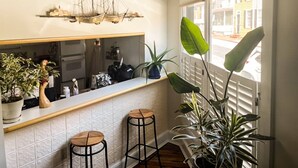 Une cuisine avec un mur recouvert de carreaux, une œuvre d’art sur le thème des navires, deux tabourets et des plantes en pot.