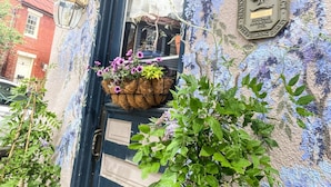 Un bâtiment avec une porte bleue, une jardinière suspendue et une plaque fixée au mur.