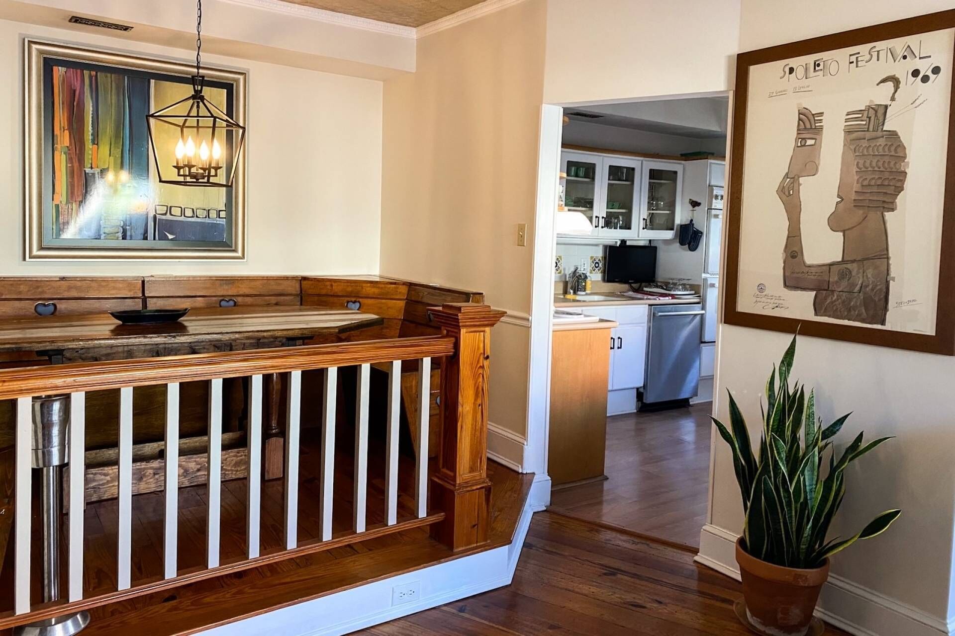 Un escalier en bois mène à une cuisine dotée de meubles blancs, à un coin repas avec un banc et à une œuvre d’art encadrée accrochée au mur.