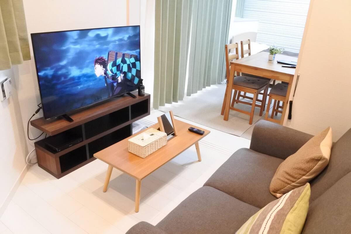 A living room with a flat-screen TV, wooden furniture, and a dining area.