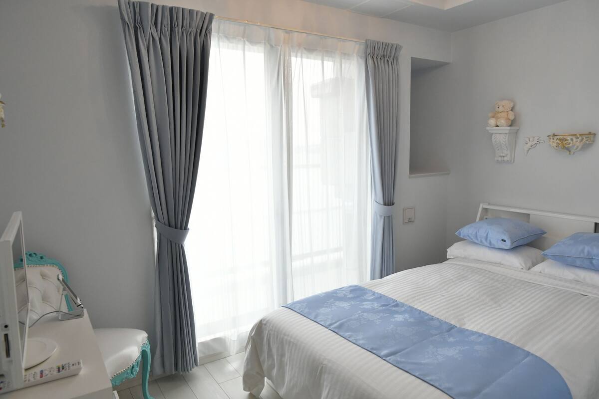A bedroom with a bed, a bedside table, a lamp, and a window with curtains.