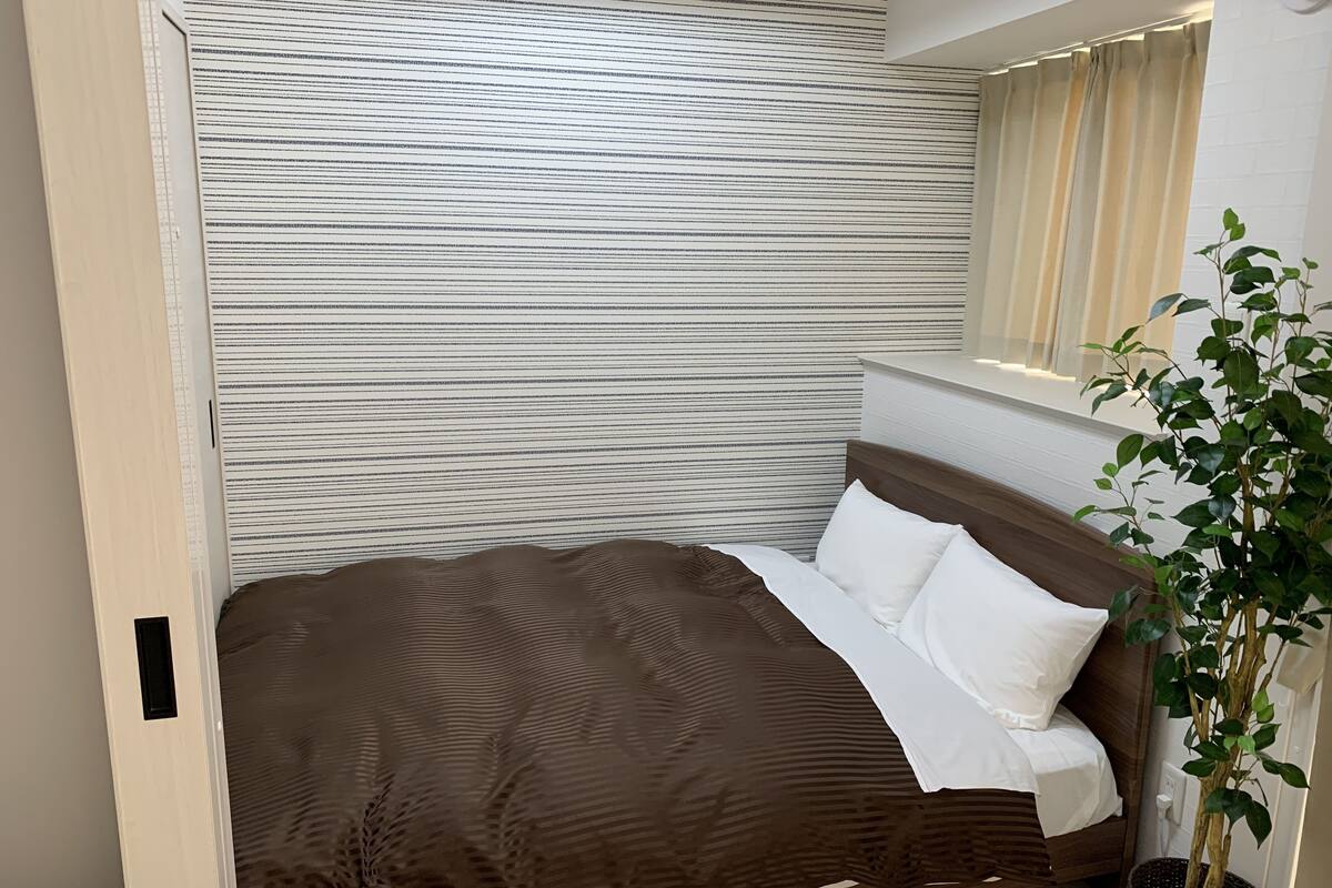 A neatly made bed with a patterned bedspread, a potted plant, and a striped wall.