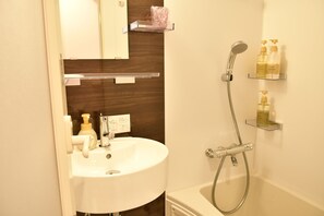 Un baño con lavamanos blanco, un espejo, ducha y estantes con artículos de aseo.