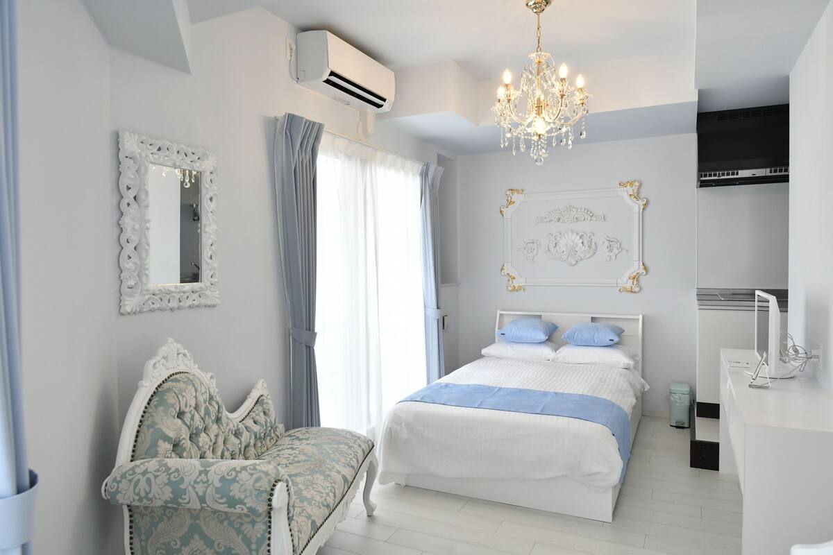 A bedroom with a bed, a chair, a desk, and a chandelier.