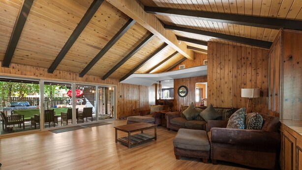 Un vaste espace de vie doté de planchers en bois, d’un grand canapé, d’une table basse et d’une porte vitrée donnant sur un espace extérieur avec une piscine.