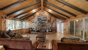 L’intérieur d’un chalet chaleureux, avec une cheminée en pierre, des poutres en bois et une grande fenêtre.