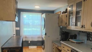 A compact kitchen with wooden cabinets, a built-in dishwasher, and a window with blinds. - The Family Escape Ranch (Erie)