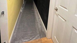 A narrow hallway with a carpeted floor, a ceiling light fixture, and a door on the right. - The Family Escape Ranch (Erie)
