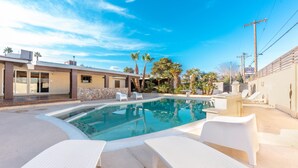Una piscina con lettini, un muro in pietra e palme.