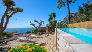 Zona de piscina con patio de piedra, sillas de descanso y vista al mar.