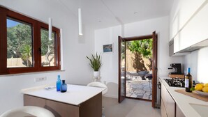 Una cocina moderna con una isla central, un comedor con sillas blancas y vistas a un patio trasero con una barbacoa.