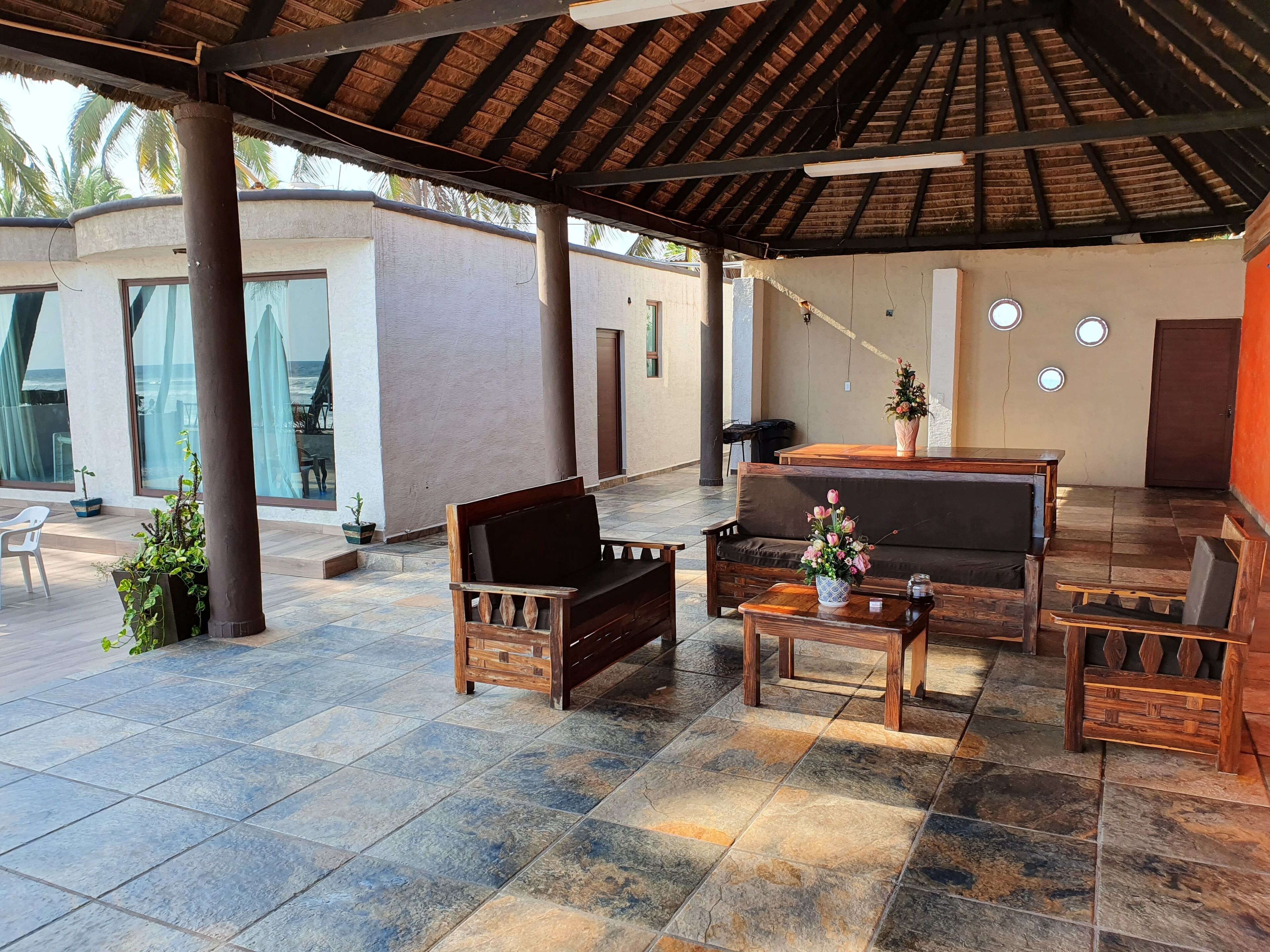 A covered outdoor seating area with wooden furniture and a tiled floor.