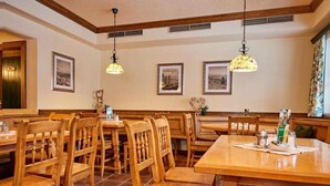 Un restaurante con mesas y sillas de madera, cuadros en las paredes y lámparas colgantes.