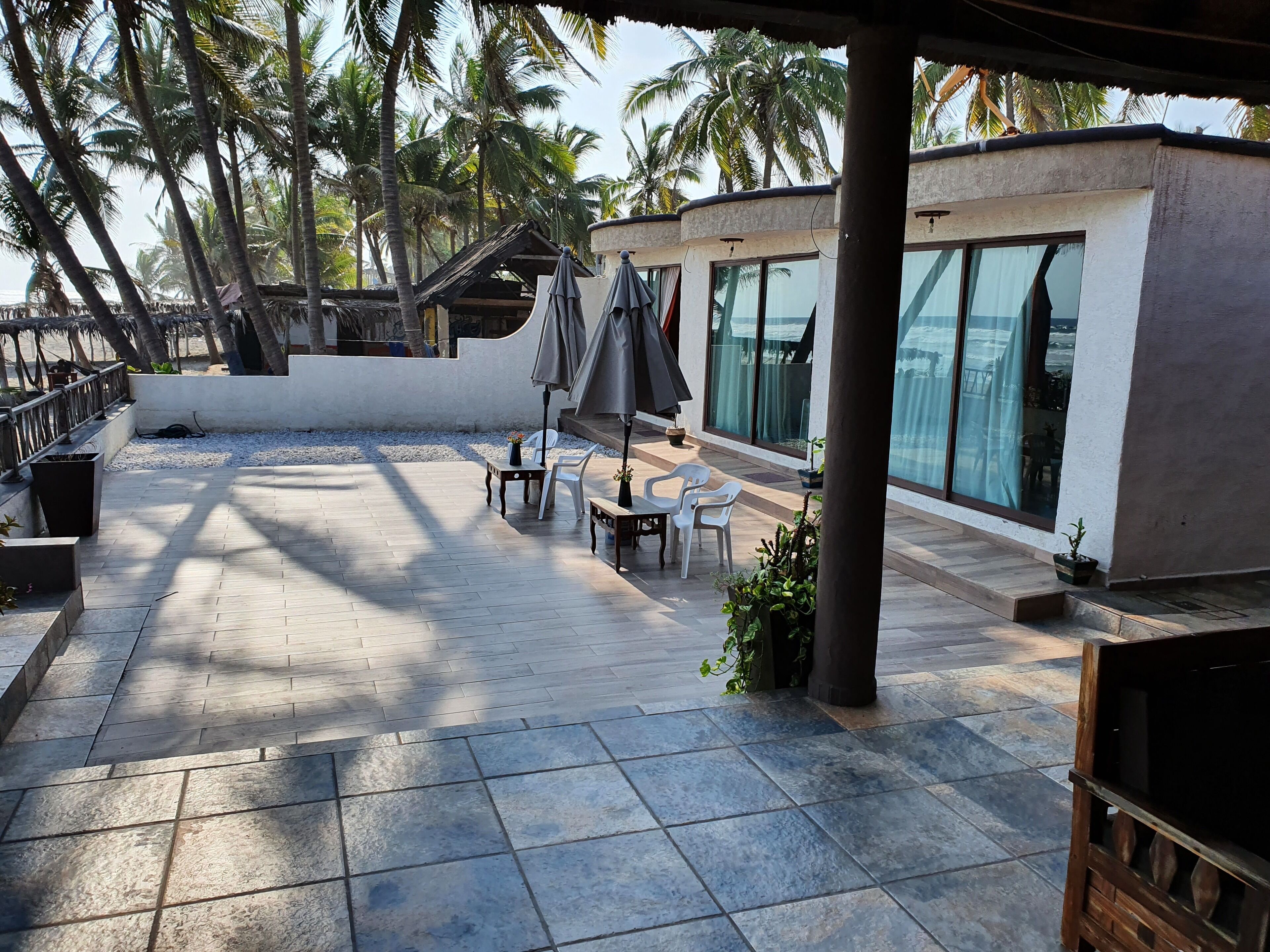 A covered outdoor patio with tiled flooring, white plastic chairs, a table, and umbrellas.