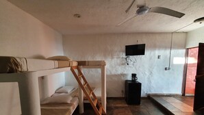 Een studentenkamer met stapelbedden, een plafondventilator, een televisie en een koffiezetapparaat.