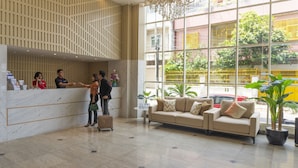 A hotel reception area with a marble counter, a sofa, and large windows with a view of the street. - d'primahotel Balikpapan (Balikpapan)