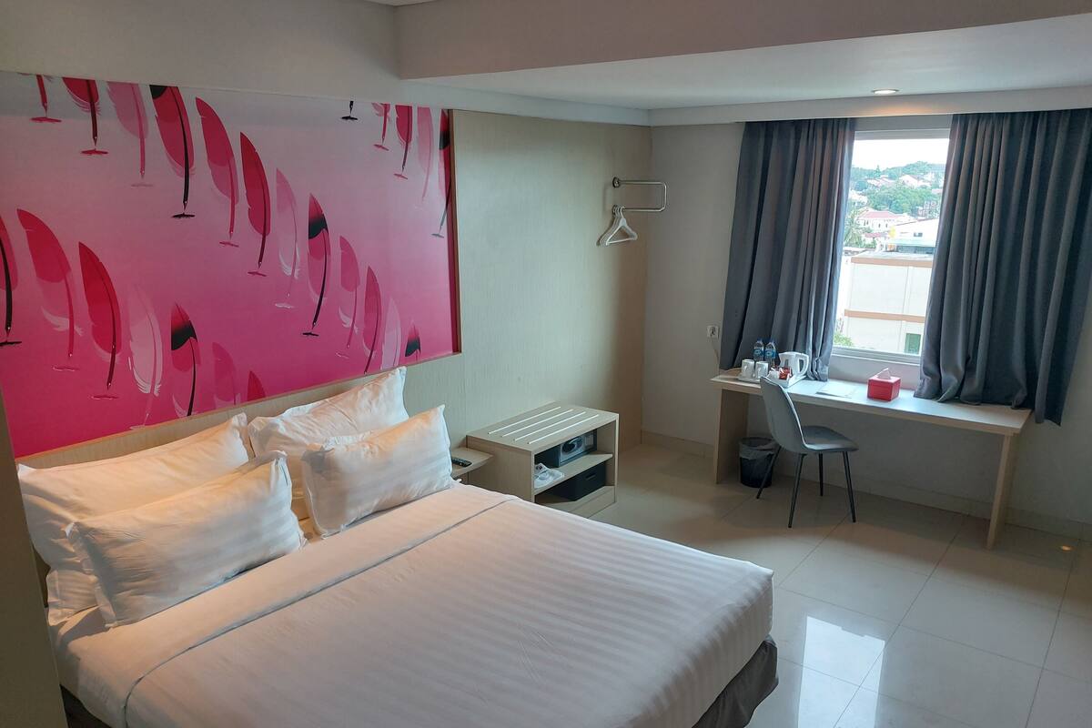 A hotel room with a bed, a desk, and a window with curtains.