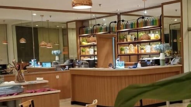A restaurant with a wooden counter, multiple tables, and chairs. - d'primahotel Balikpapan (Balikpapan)