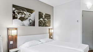 Une chambre d’hôtel avec un grand lit, deux lampes fixées au mur et deux tableaux encadrés accrochés au mur.