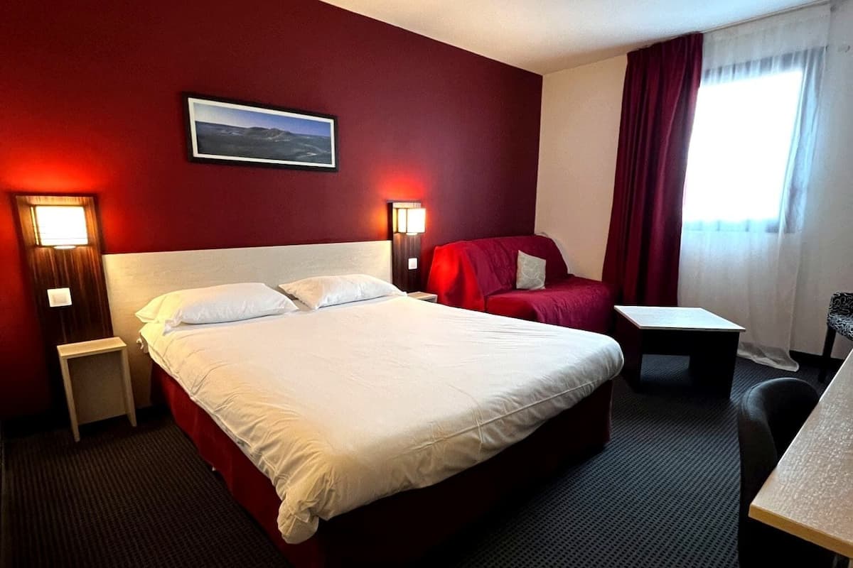 Een hotelkamer met een groot bed, een bureau, een stoel en twee bedlampjes.