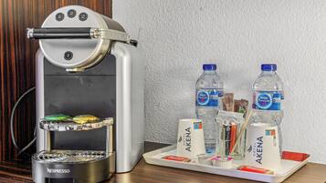 Una cafetera Nespresso con una bandeja de vasos desechables, dos botellas de agua y una pequeña variedad de bocadillos.