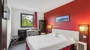 Une chambre d’hôtel équipée d’un lit, d’un bureau, d’une chaise, d’une télévision et d’une fenêtre donnant sur un paysage verdoyant.