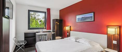 Habitación de hotel con cama, escritorio, silla, televisión y ventana con vistas a zonas verdes.