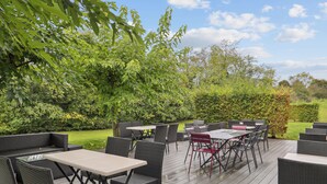 Une terrasse extérieure aménagée avec des meubles et des tables en osier, entourée d’une végétation luxuriante et d’arbres.