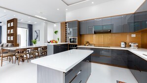 A modern kitchen with a central island, built-in appliances, and a dining area with wooden chairs and a white table. - Tran Duy Sunrise Villa (Ho Chi Minh City)