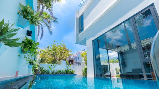 A modern pool area with a clear blue pool, surrounded by lush greenery and a white building with large windows. - Tran Duy Sunrise Villa (Ho Chi Minh City)
