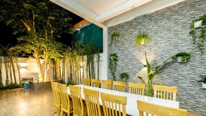 A dining area with a long table and wooden chairs, surrounded by a stone wall with plants. - Tran Duy Sunrise Villa (Ho Chi Minh City)