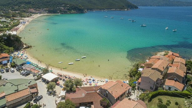 Un pueblo costero con playa, aguas turquesas cristalinas y barcos.