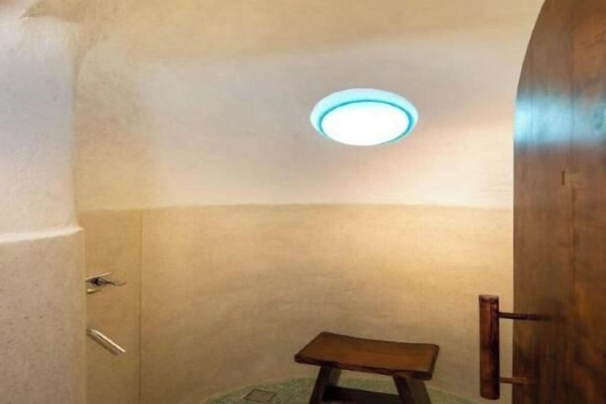 A small, enclosed bathroom with a bench, a door, and a ceiling light.