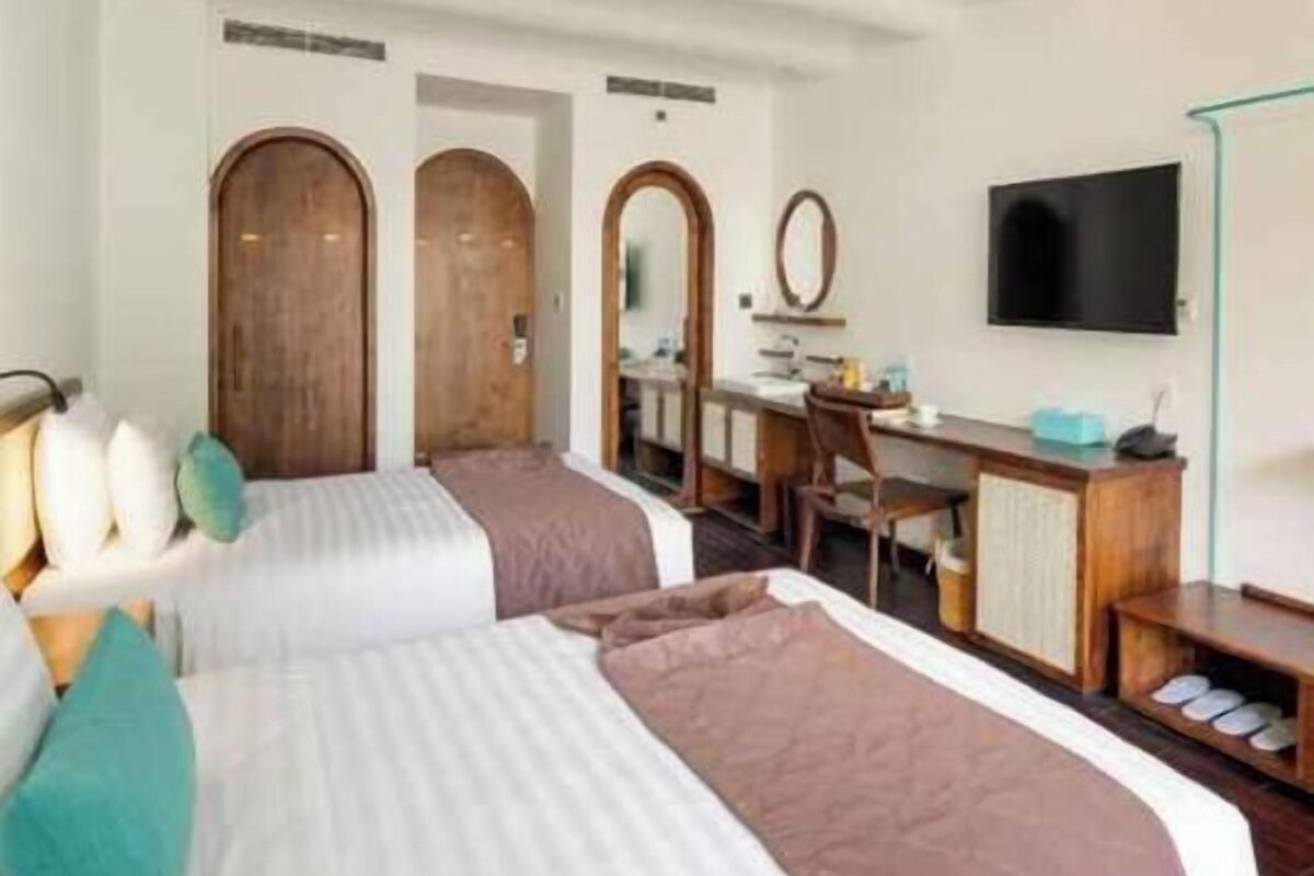 A hotel room with two beds, a desk, a chair, a television, and a wardrobe.