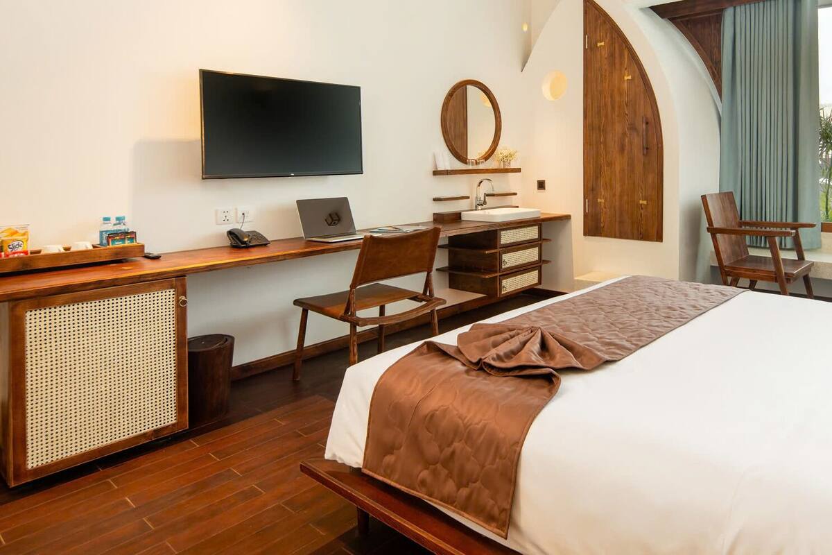 Une chambre d’hôtel équipée d’un lit, d’un bureau, d’une chaise, d’une télévision et d’une fenêtre donnant sur un paysage verdoyant.