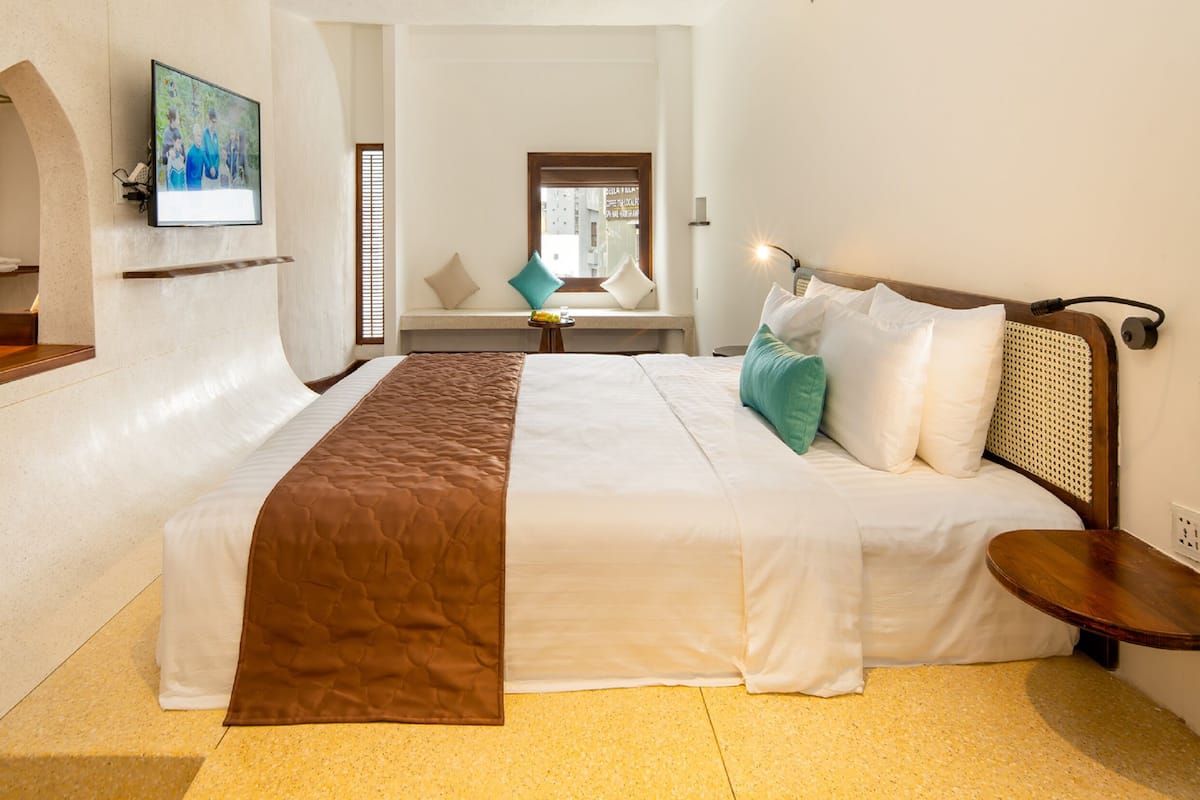 Une chambre d’hôtel avec un grand lit, un téléviseur fixé au mur, une petite table et un banc.